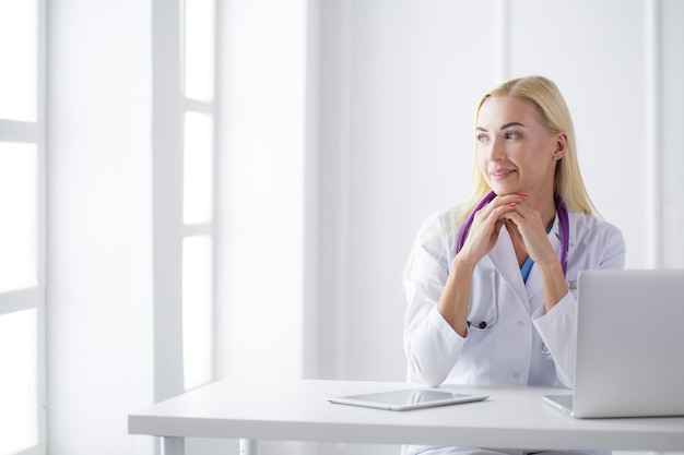 Female doctor sitting on the desk and working a laptop in hospital