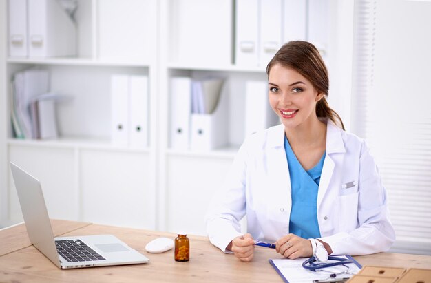 Female doctor sitting on the desk and working a laptop