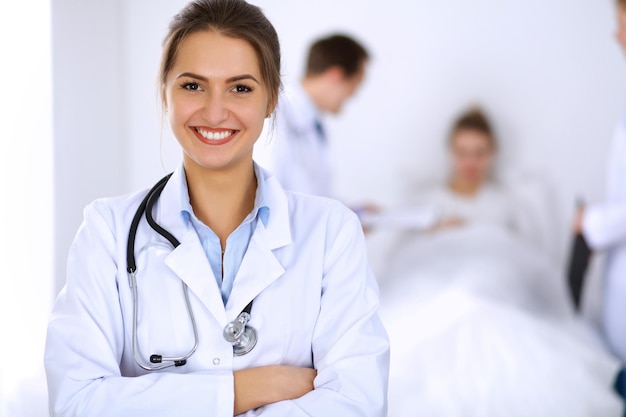 Female doctor smiling on the background with patient in the bed and two doctors.