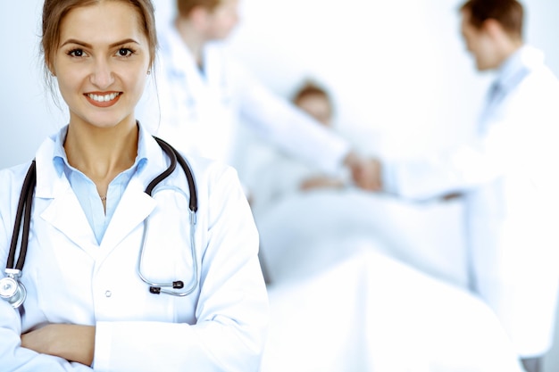 Female doctor smiling on the background with patient in the bed and two doctors.