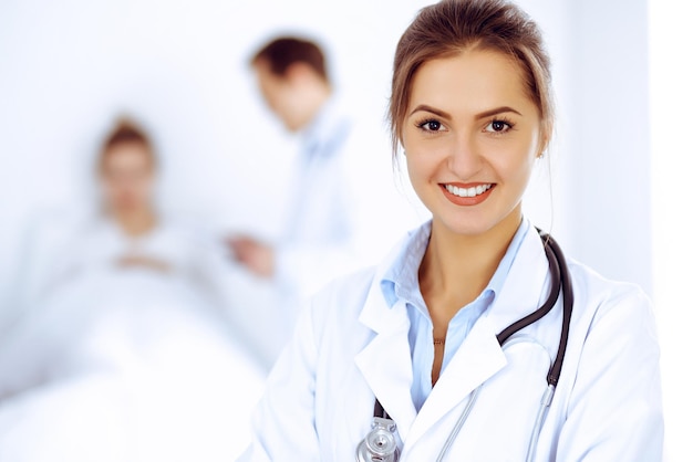 Female doctor smiling on the background with patient in the bed and two doctors.