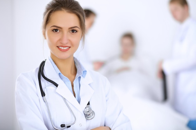 Female doctor smiling on the background with patient in the bed and two doctors.