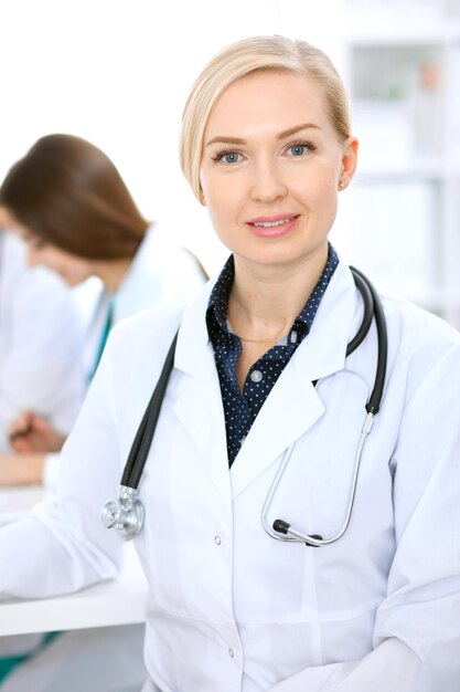 Female doctor smiling on the background with patient and his physician in hospital.