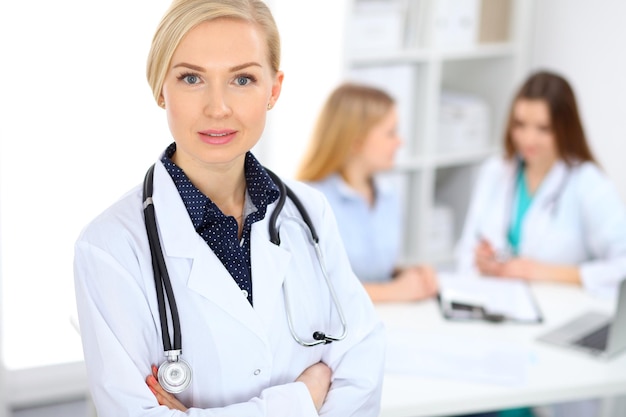 Female doctor smiling on the background with patient and his physician in hospital.