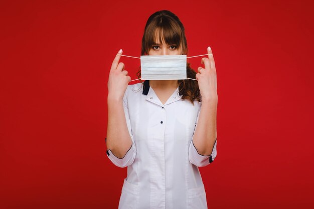 A female doctor stands in a medical mask isolated on a red background.