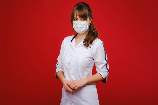 A female doctor stands in a medical mask isolated on a red