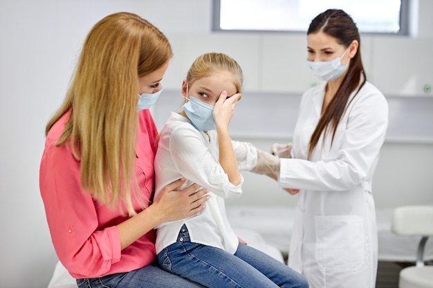 クリニックで少女の血液サンプル検査を受ける女性医師、怖がっている少女は母親と一緒に座り、女性技術者は採血の実験室で子供に血液検査を行います