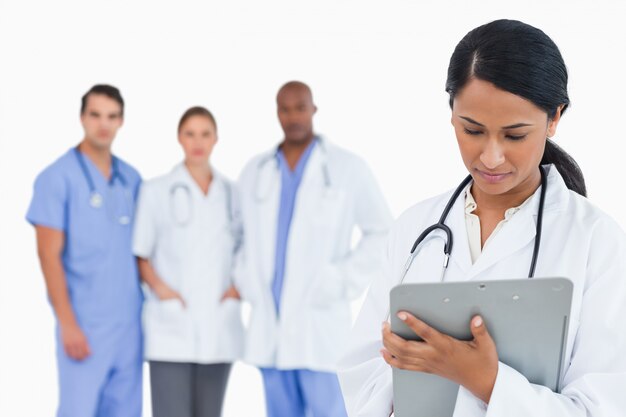 Female doctor taking notes on clipboard with staff members behind her