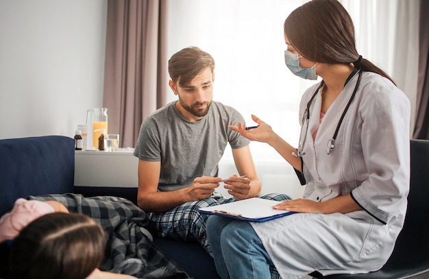 Female doctor talk to young man. Sick girl lying on couch besides. Doctor explain him.