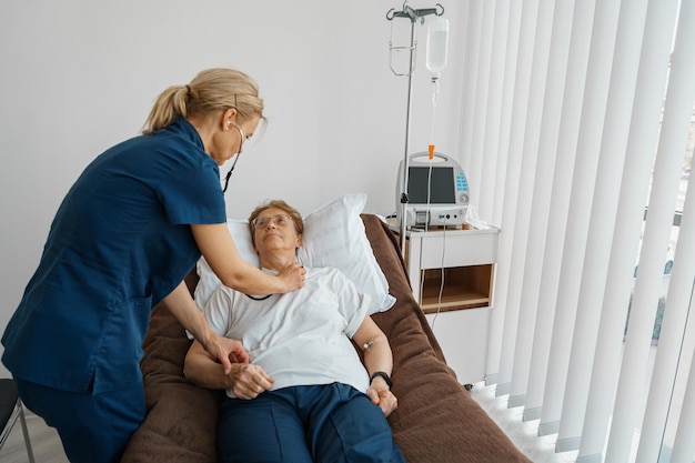 Foto terapista medico femminile che ascolta la respirazione paziente della donna anziana facendo uso dello stetoscopio