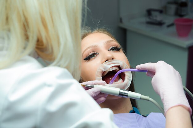 Female doctor in uniform checking up female patient's teeth in dental clinic.