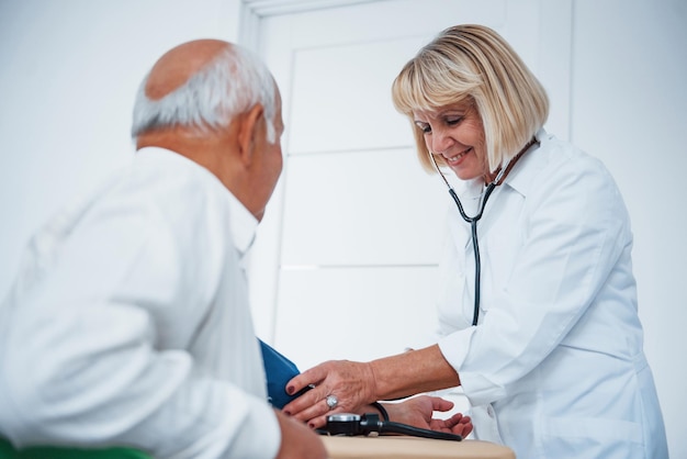 Photo female doctor uses tonometer to make blood pressure measuring to senior man