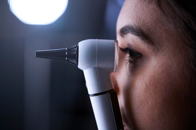 Женщина-врач использует отоскоп для осмотра сбоку