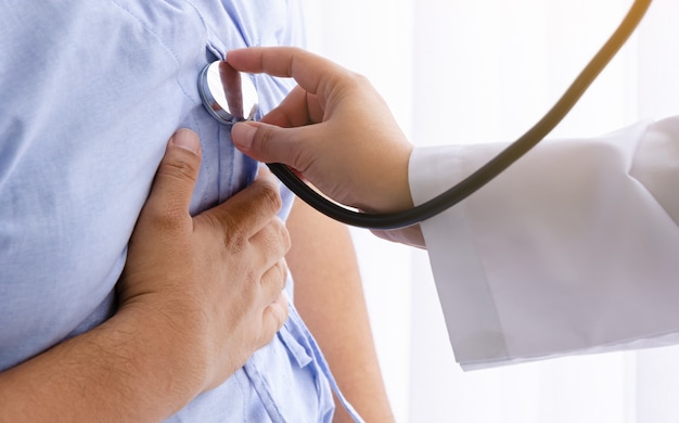 Female doctor using a stethoscope to listen to male patient\'s\
heartbeat with heart attack in hospital room