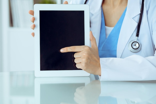 Female doctor using tablet computer while sitting at the workplace, close-up of hands. Medicine, healthcare and help concept.