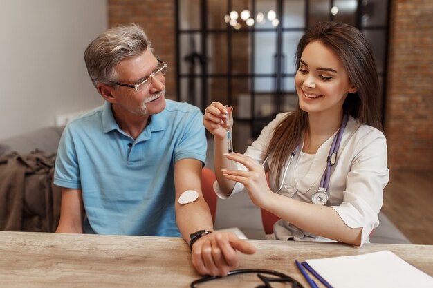 The female doctor vaccinates to the old patient at home