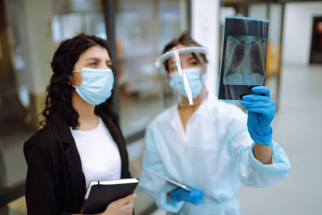 A female doctor in visor and protective gloves examines an X-ray of a patient