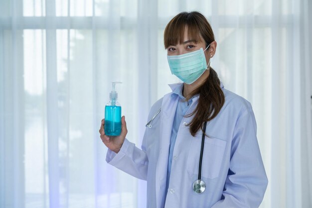 La dottoressa indossa un'uniforme bianca e una maschera facciale con una bottiglia di alcol gel