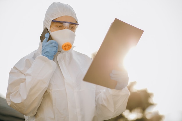 Female Doctor Wearing a Facemask and Suit Stands Outside in the Sunset. Nurse wears a protective suit and mask during the COVID19 outbreak. Doctor epidemiologist fighting with coronavirus COVID-19.