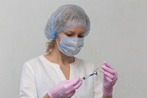 A female doctor, wearing gloves and a mask, fills a syringe with medicine, close-up. Covid-19 Vaccination