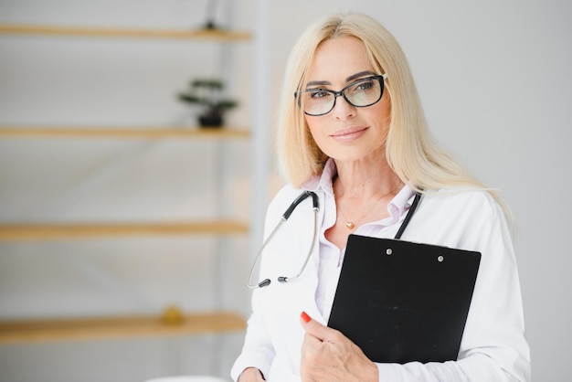 Female doctor wearing lab coat and stethoscope and holding clipboard in her hands while standing at hospital