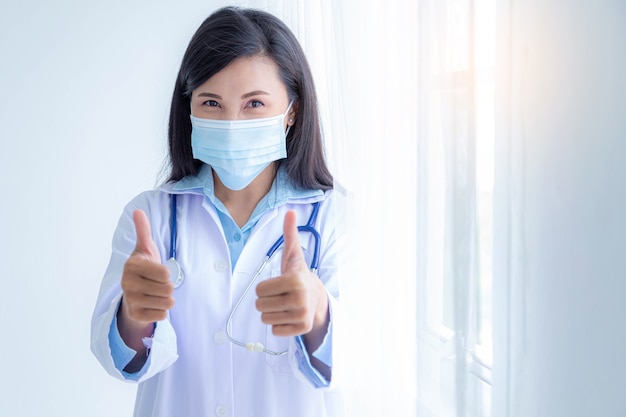 엄지손가락을 보여주는 의료 마스크를 쓰고 여성 의사. 코로나 바이러스 감염병 세계적 유행. 코로나 19 발생.