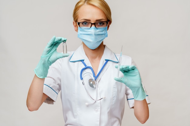 보호 마스크와 장갑을 착용하고 백신 약과 주사기의 병을 들고 여성 의사