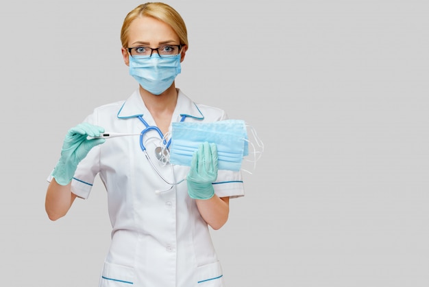 Female doctor wearing protective mask and gloves and holding electronic thermometer