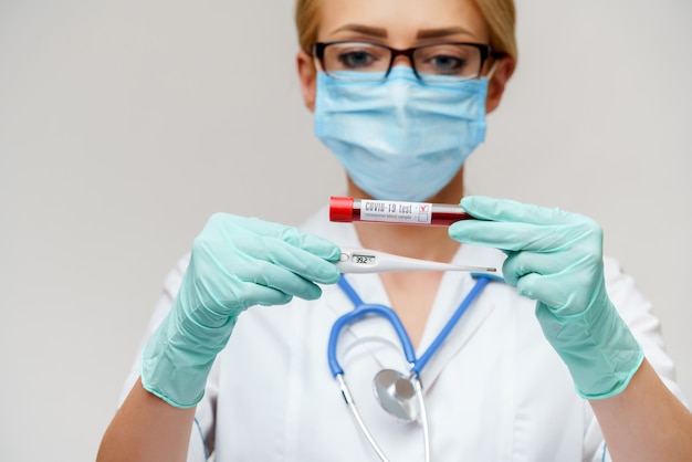 Женщина-врач в защитной маске и перчатках с электронным термометром