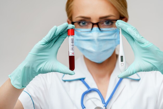 Female doctor wearing protective mask and gloves and holding electronic thermometer