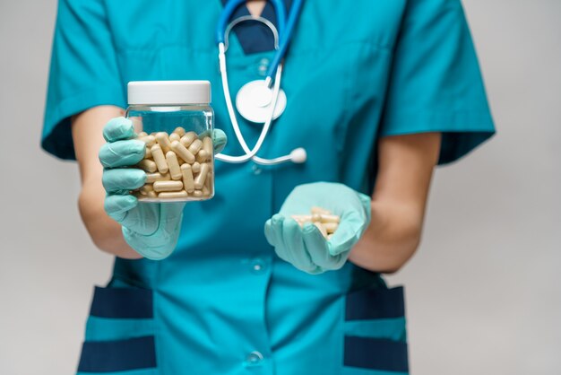 Female doctor wearing protective mask and latex gloves holding pills