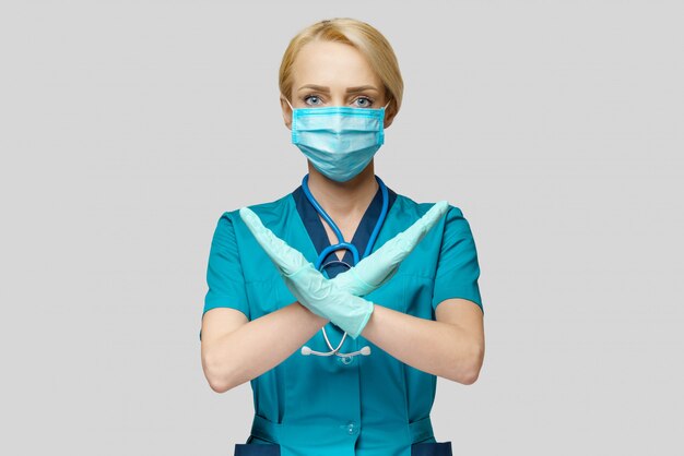 Female doctor wearing protective mask and latex gloves stop sign gesture