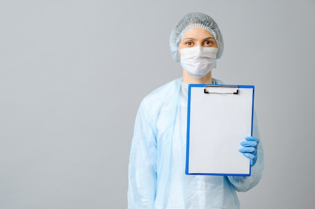 Female doctor wearing protective mask showing clipboard with white paper. Isolated on gray