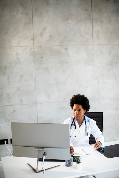 Female  doctor wearing white coat with stethoscope sitting behind desk in the office