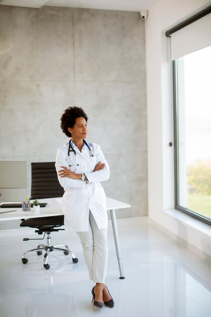 Female  doctor wearing white coat with stethoscope standing by desk in the office