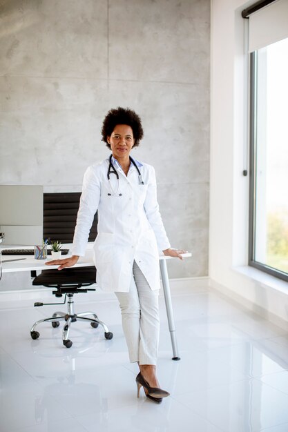 Female  doctor wearing white coat with stethoscope standing by desk in the office