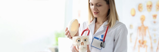 Female doctor in white coat is holding dummy of human skull