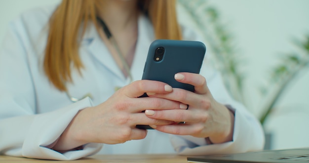 Female doctor in white coat using modern smartphone device