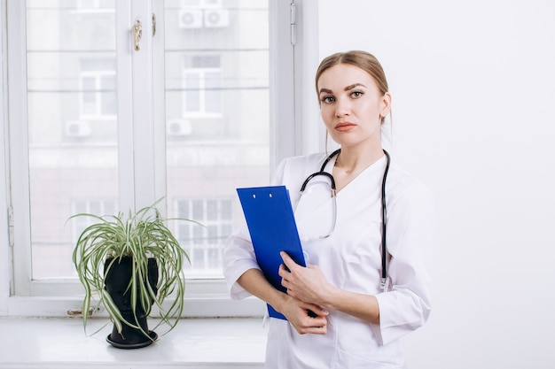 Female doctor in white coat with stethoscope and blue folder