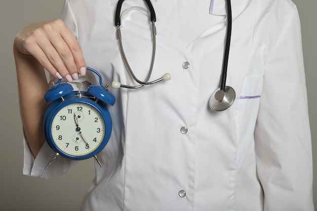 Female doctor with clock, standing on grey background