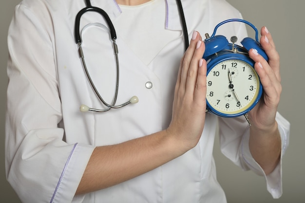 Female doctor with clock, standing on grey background