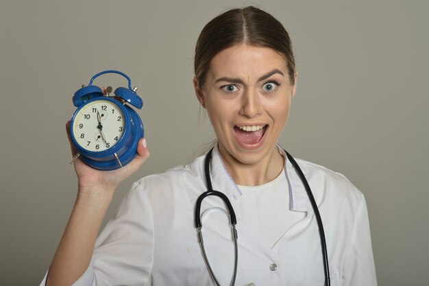 Female doctor with clock, standing on grey background