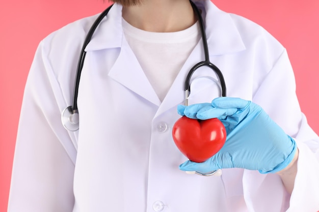 Female doctor with heart on pink background, close up