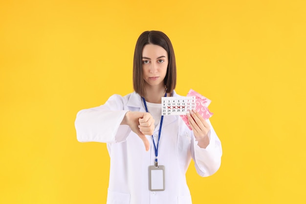 Женщина-врач с периодическим календарем и подушечками на желтом фоне