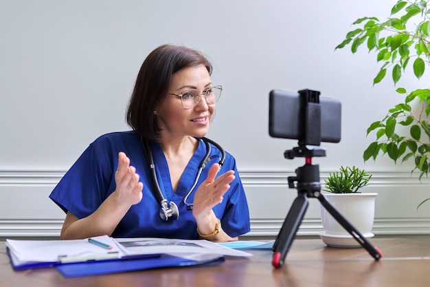 Female doctor with a stethoscope consulting online using a smartphone on a tripod