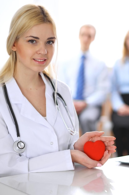 Foto medico femminile con lo stetoscopio che tiene il cuore. coppia di pazienti seduti in background