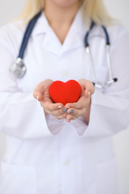 Female doctor with stethoscope holding heart.  Patients couple sitting in the background