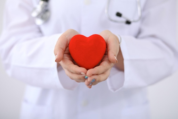 Female doctor with stethoscope holding heart.  Patients couple sitting in the background