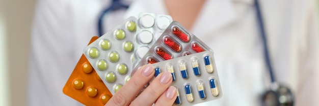 Female doctor with stethoscope holds blister packs of pills and vitamins in hand specialist