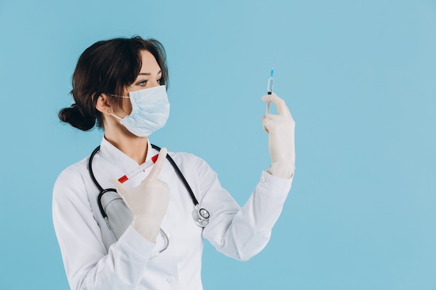 Female doctor with stethoscope in mask holding injection, antidote against coronavirus